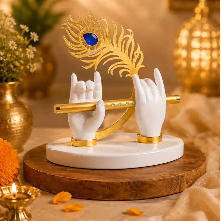 A decorative white and gold flute holder sculpture with two sculpted hands holding a gold flute, topped with a gold peacock feather featuring a blue jewel, displayed on a round wooden base in a warm, styled indoor setting.