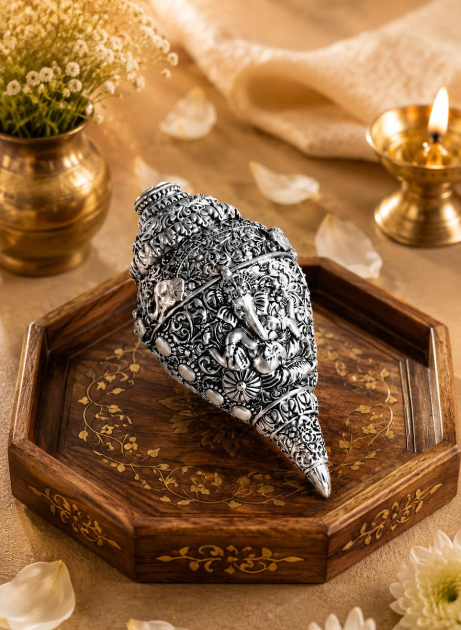 A black and white patterned shell sculpture displayed on an octagonal wooden tray with gold detailing, set against a warm neutral background with dried flowers, petals, and a brass candle holder.